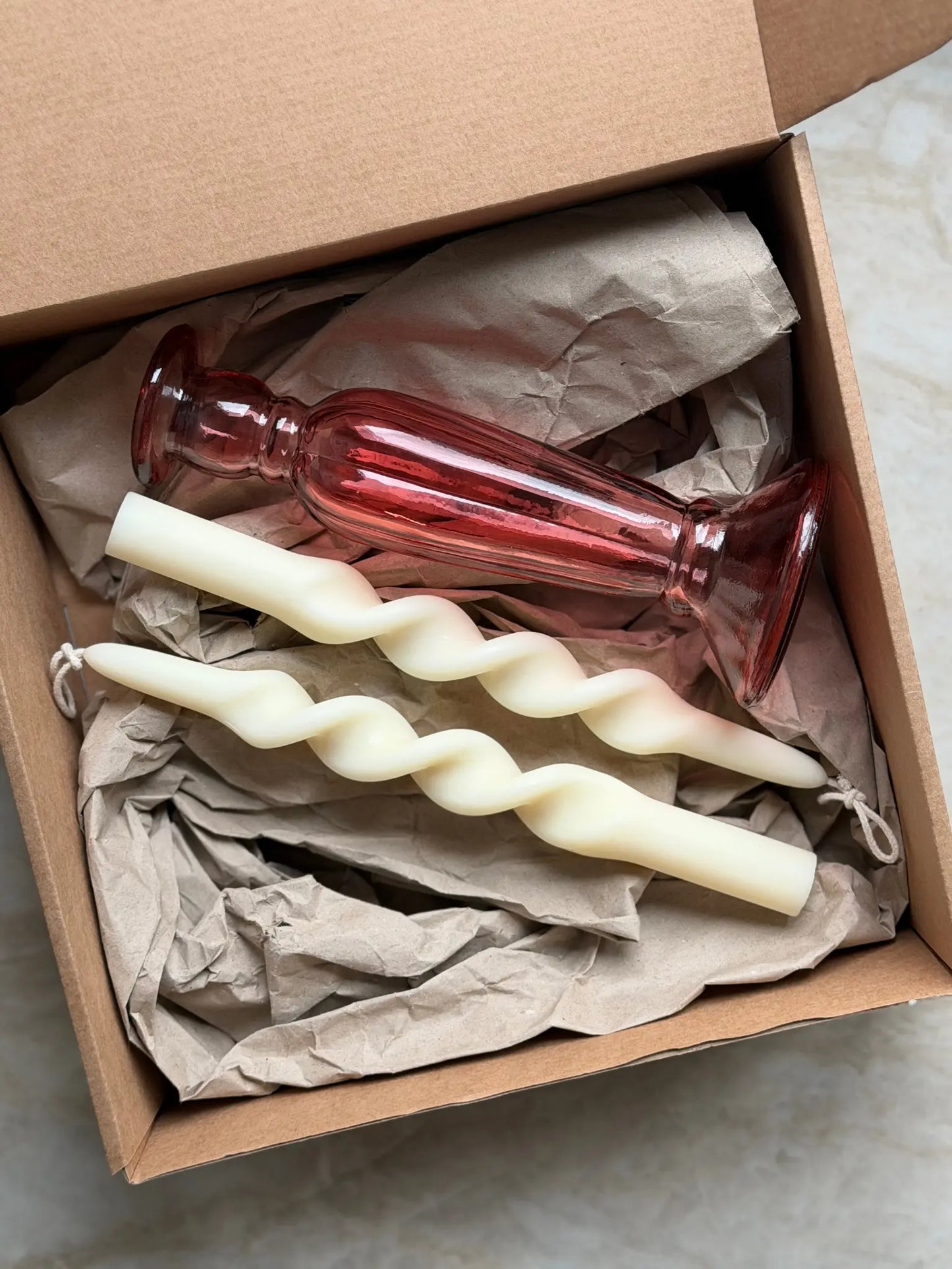 Geschenkset bestehend aus einem 2er-Set kleiner, gedrehter Stabkerzen und einem rosafarbenen Kerzenhalter aus Recycling-Glas