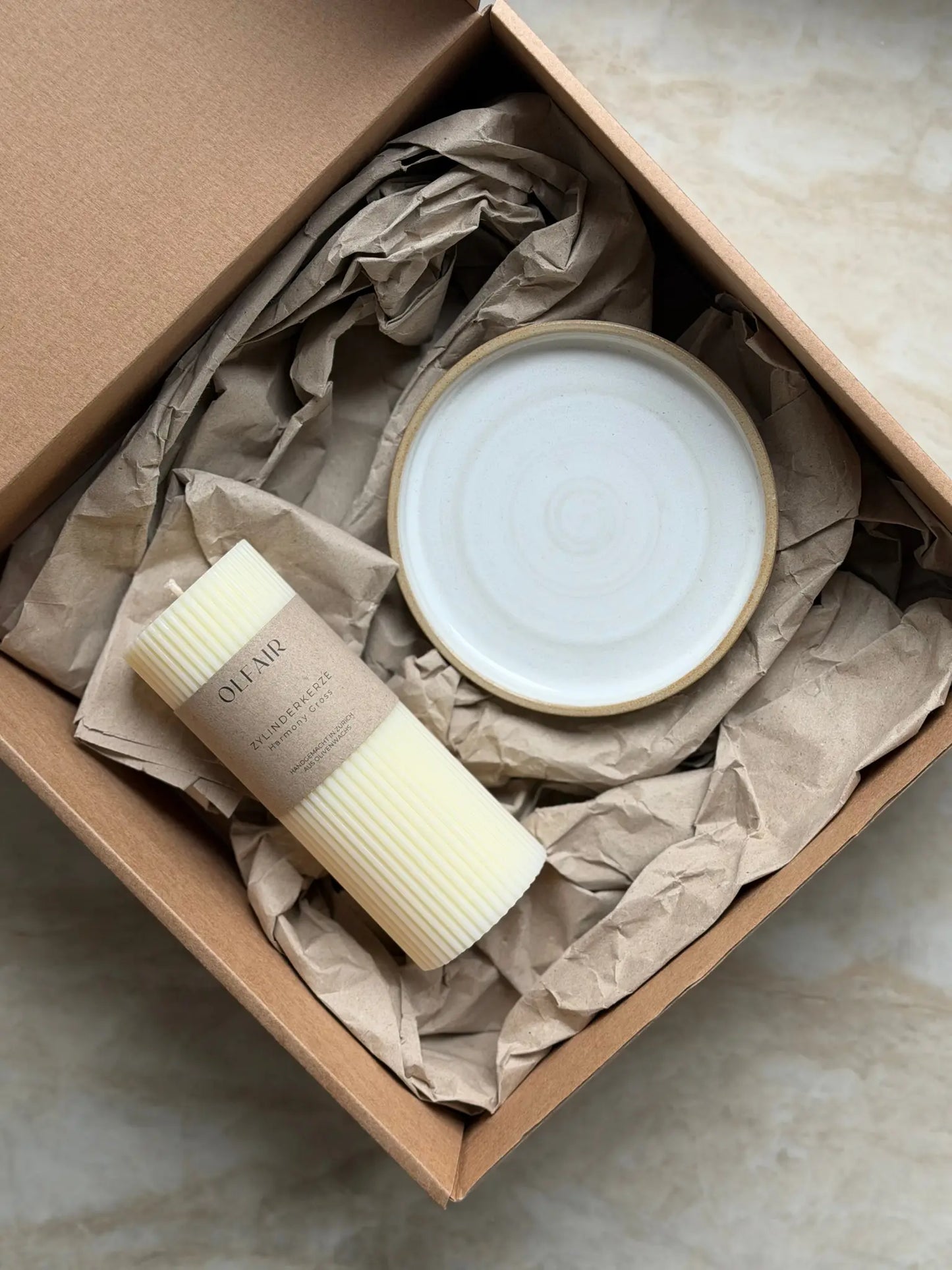 Geschenkset mit einer grossen Zylinderkerze mit feinen Rillen und einem Kerzenteller aus Keramik in einer Kartonbox.