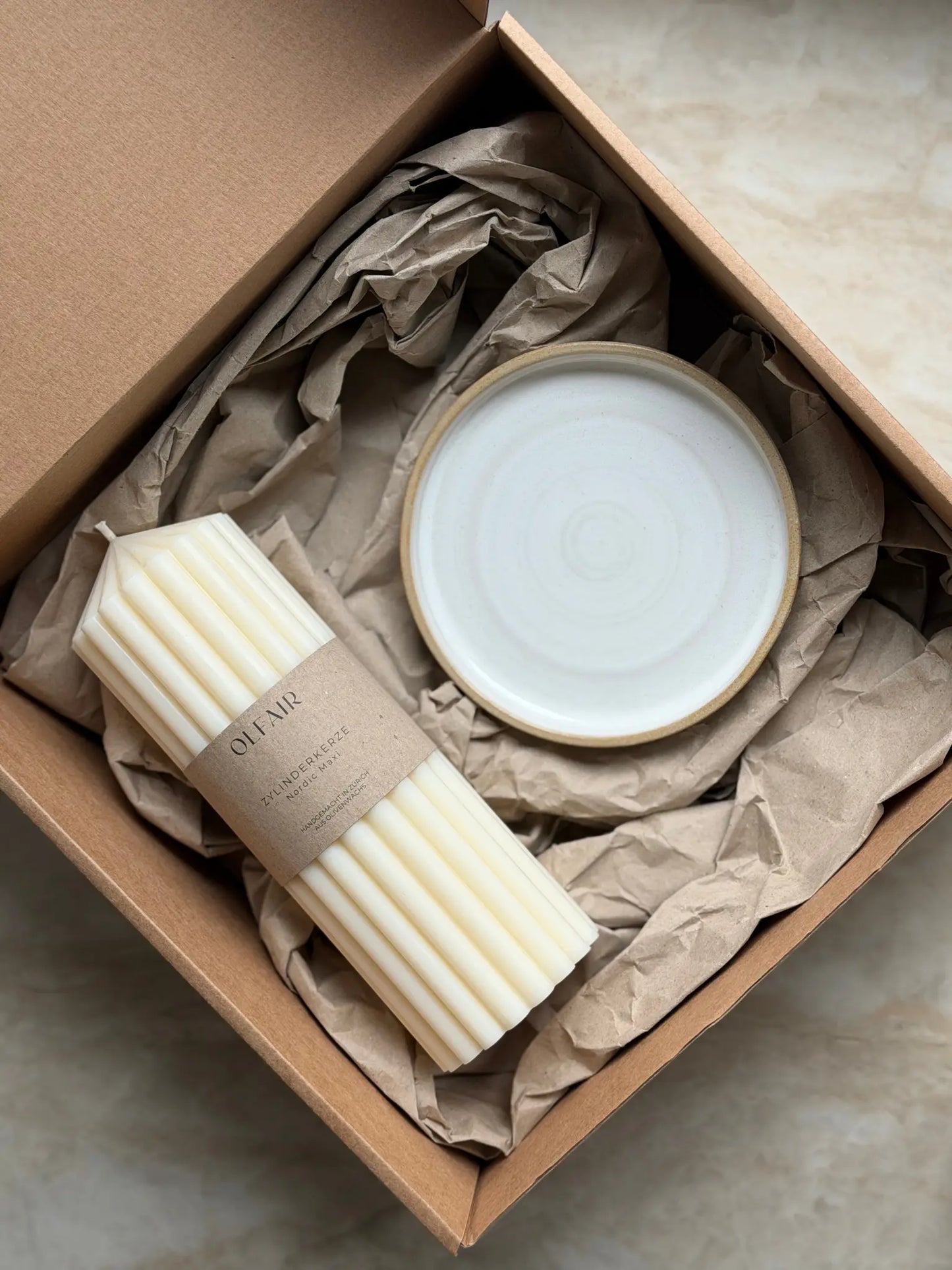 Geschenkset mit einer grossen Zylinderkerze mit breiten Rillen und einem Kerzenteller aus Keramik in einer Kartonbox.