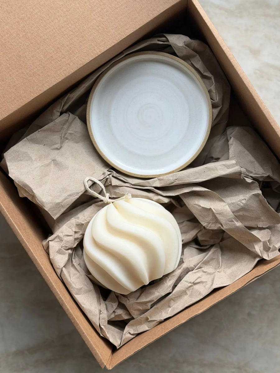 Geschenkset mit einer wellenförmigen Dekokerze und einem Kerzenteller aus Keramik in einer Kartonbox.