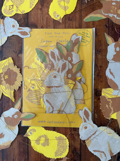 Verpackung einer Ostergirlande mit Häschen, Küken und Osterglocken. Um die Verpackung ist die Girlande verteilt.