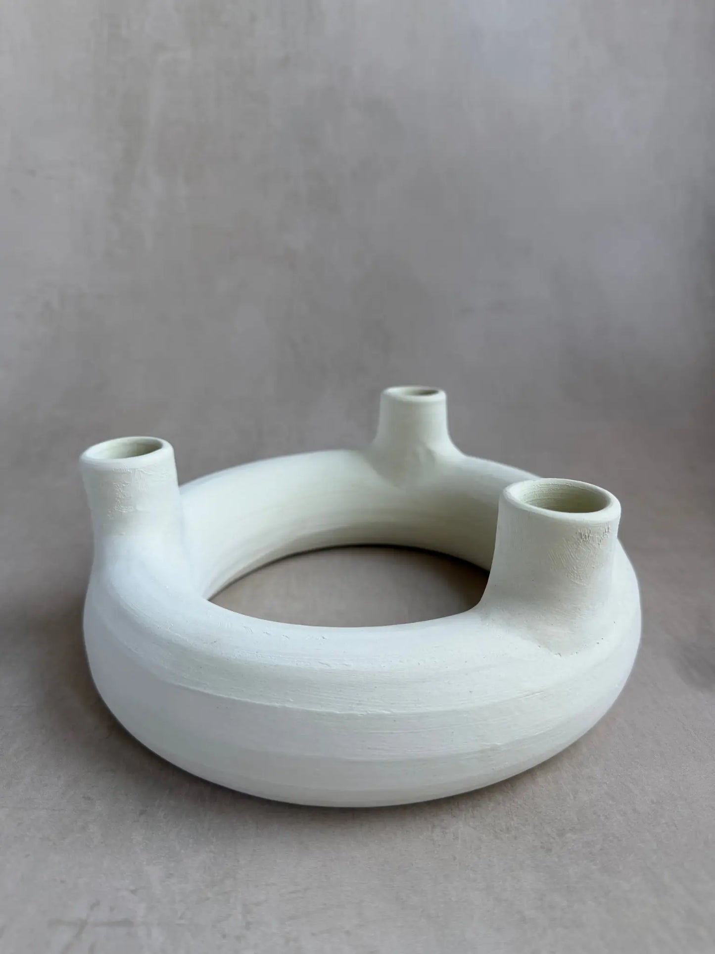 Runder Kerzenhalter mit Löchern für drei Kerzen aus unglasierter Keramik in off-white.