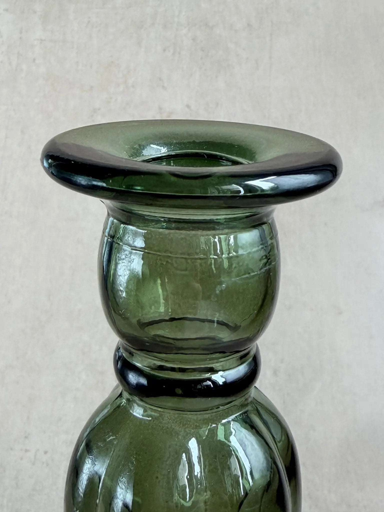 Nahaufnahme eines grünen Kerzenhalters aus Recyclingglas auf einem beigen Hintergrund.