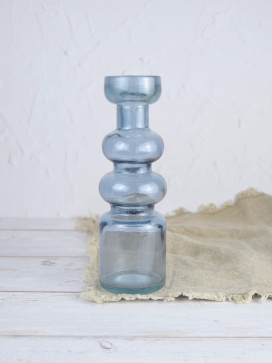 Blauer, gewölbter Kerzenhalter auf einem braunen Tuch vor einem weissen Hintergrund
