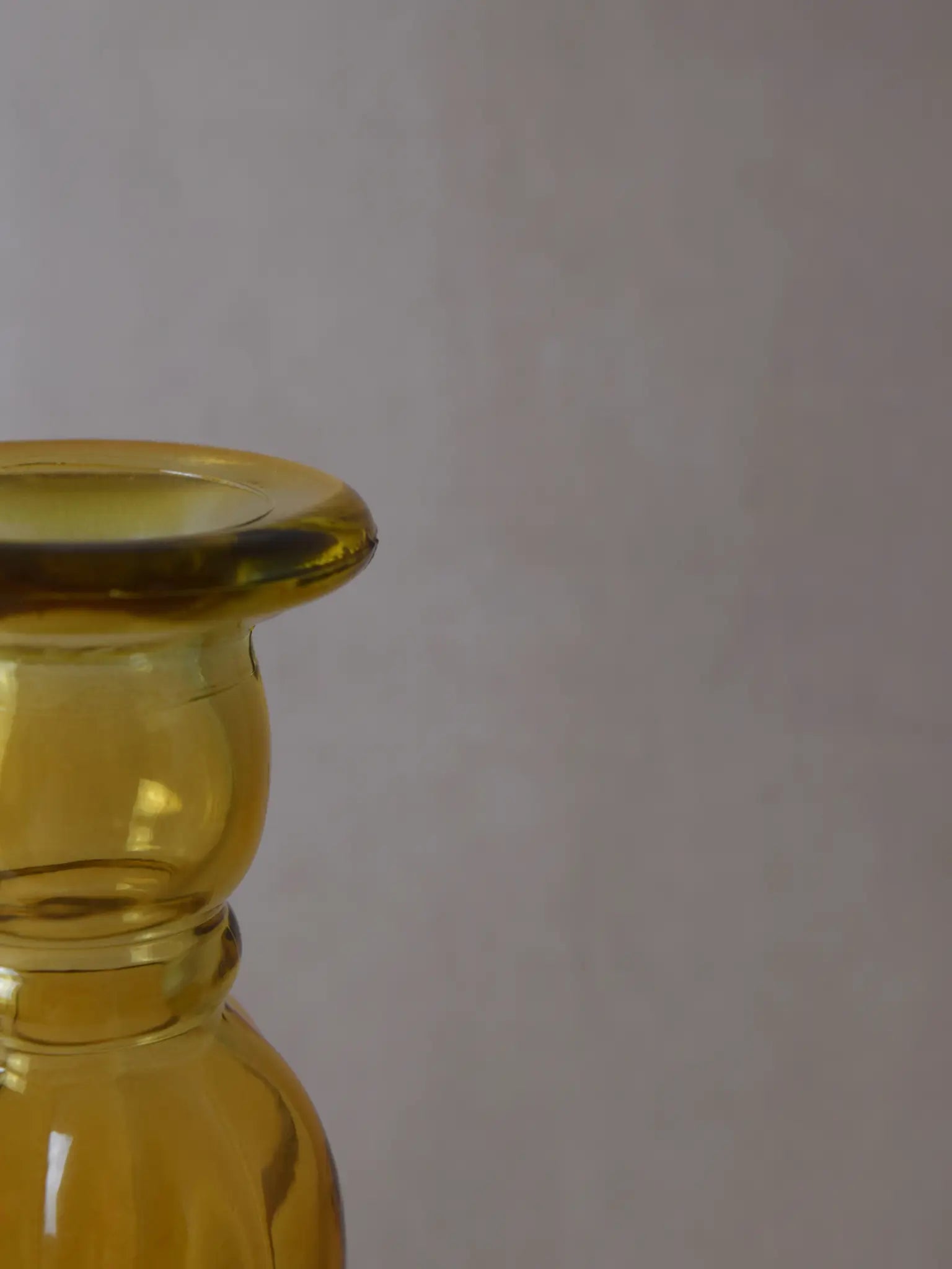 Teilaufnahme eines senfarbigen Kerzenhalters aus Recyclingglas auf einem beigen Hintergrund.