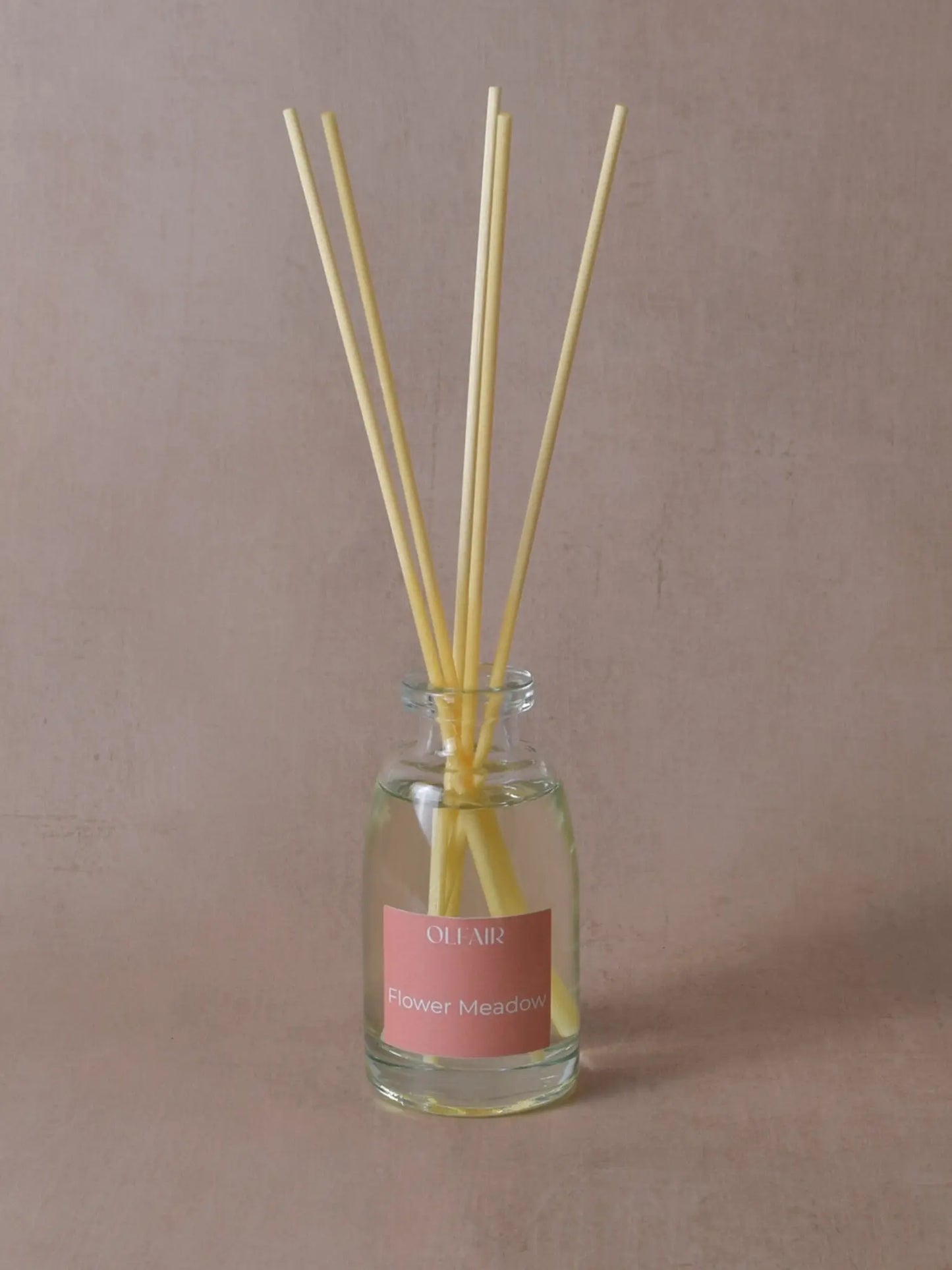 Kleiner Raumduft mit Stäbchen und einem dunkel rosa Etikett vor einem beigen Hintergrund.