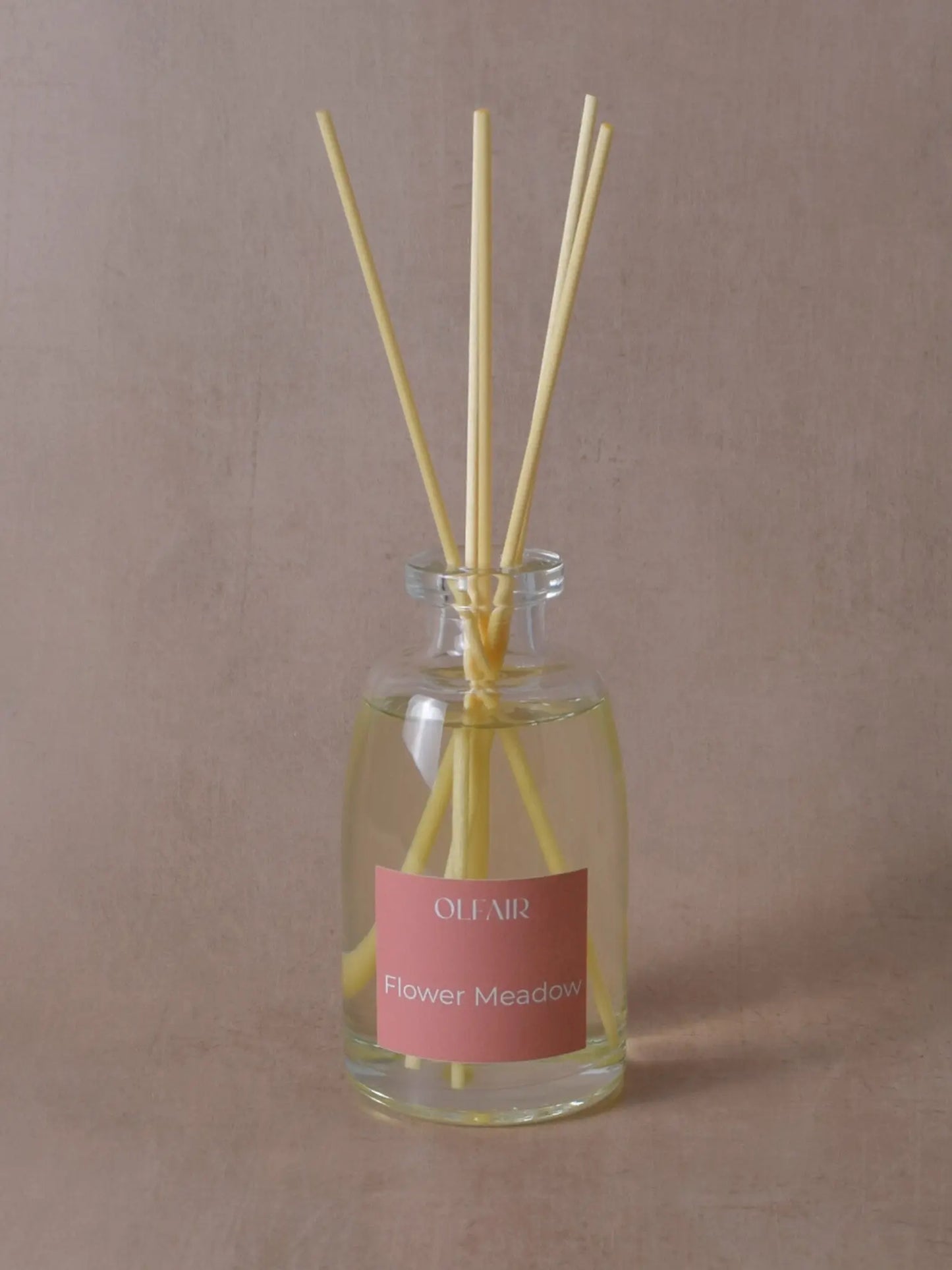 Grosser Raumduft mit Stäbchen und einem dunkel rosa Etikett vor einem beigen Hintergrund.