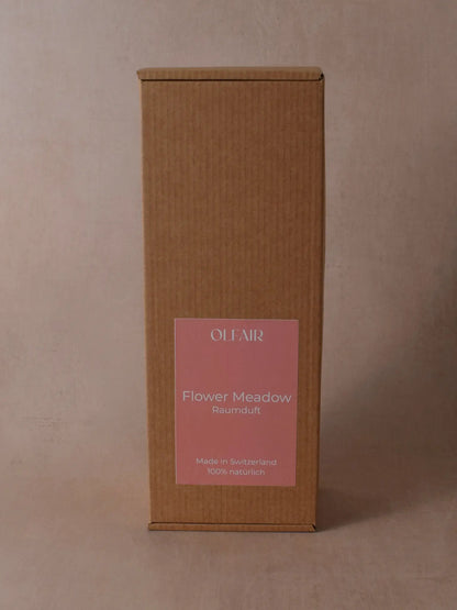 Kartonbox für Raumduft mit dunkel rosa Etikett vor einem beigen Hintergrund.