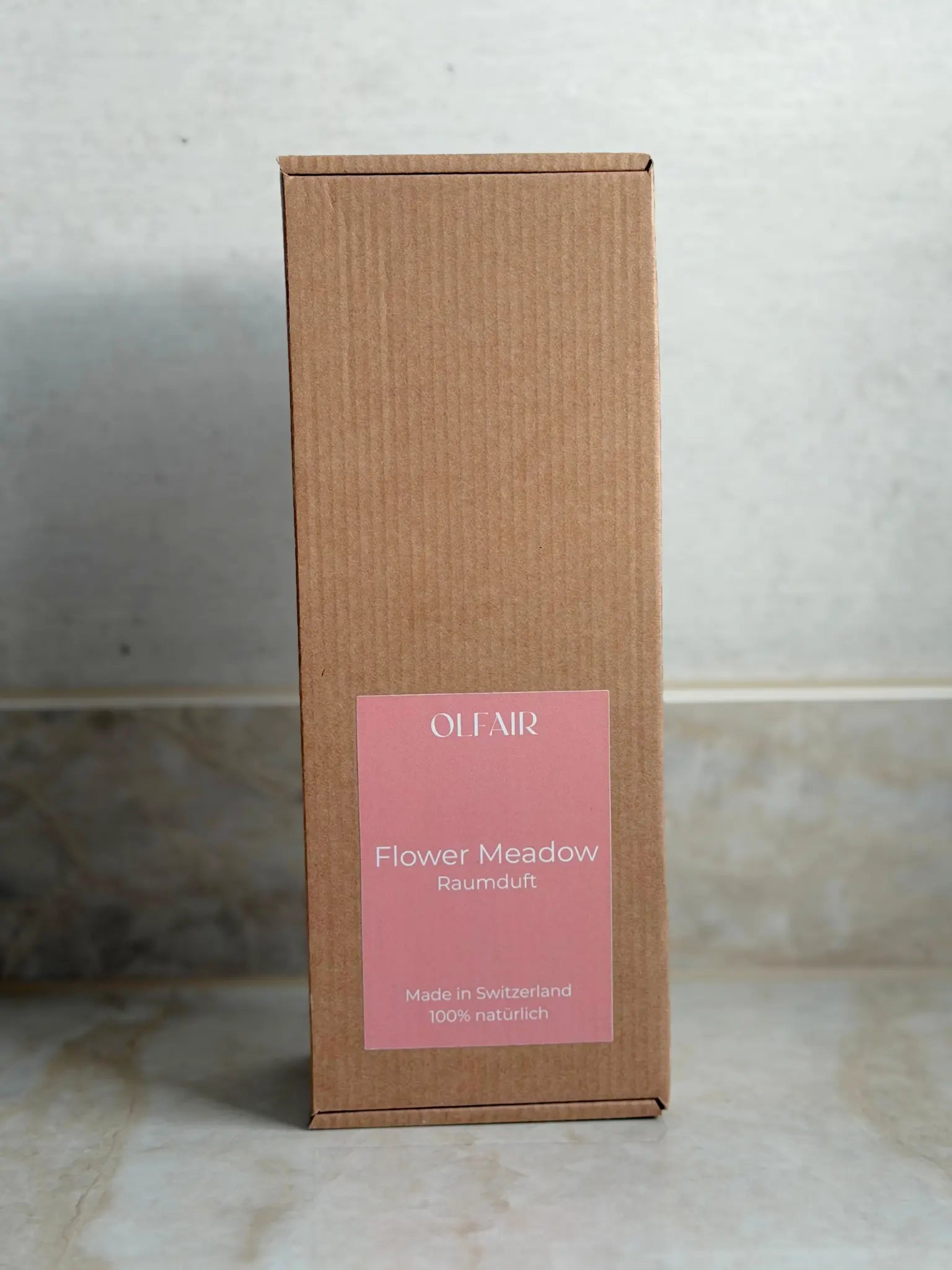 Kartonbox für Raumduft mit dunkel rosa Etikett vor einem Marmor Hintergrund.