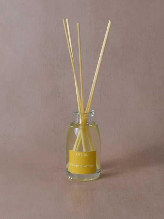 Kleiner Raumduft mit Stäbchen und einem gelben Etikett vor einem beigen Hintergrund.