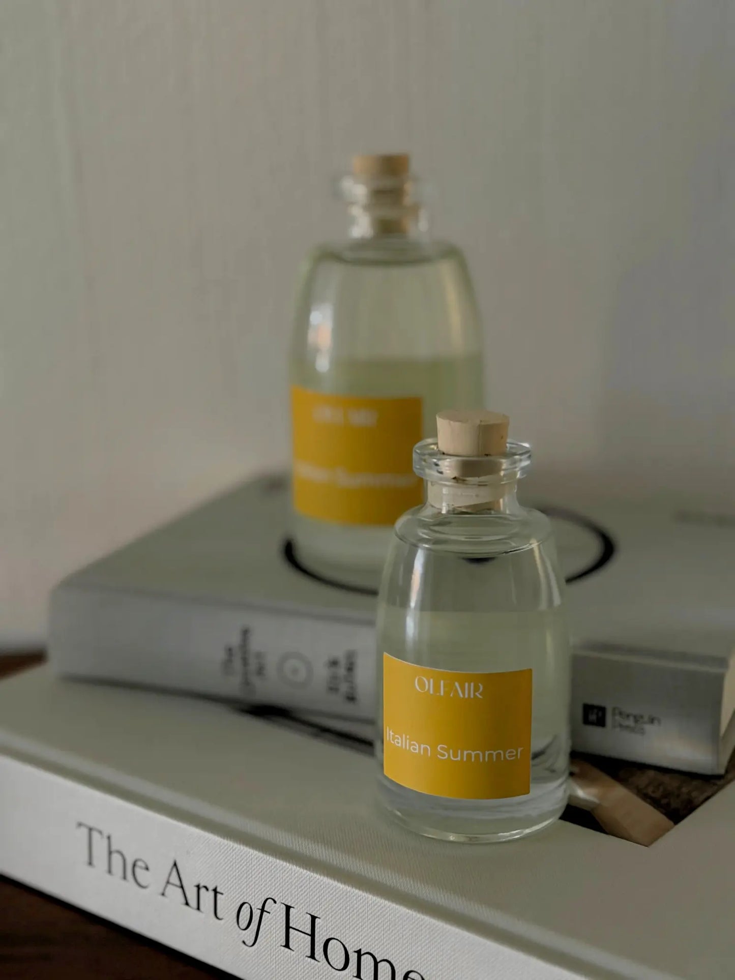 Eine kleine und eine grosse Raumduftflasche mit gelbem Etikett auf zwei Bücher.