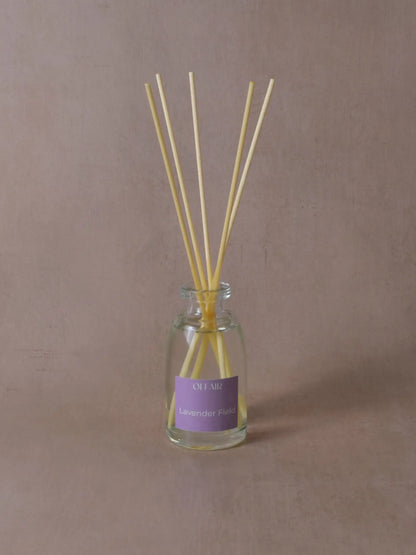 Kleiner Raumduft mit Stäbchen und einem violetten Etikett vor einem beigen Hintergrund.