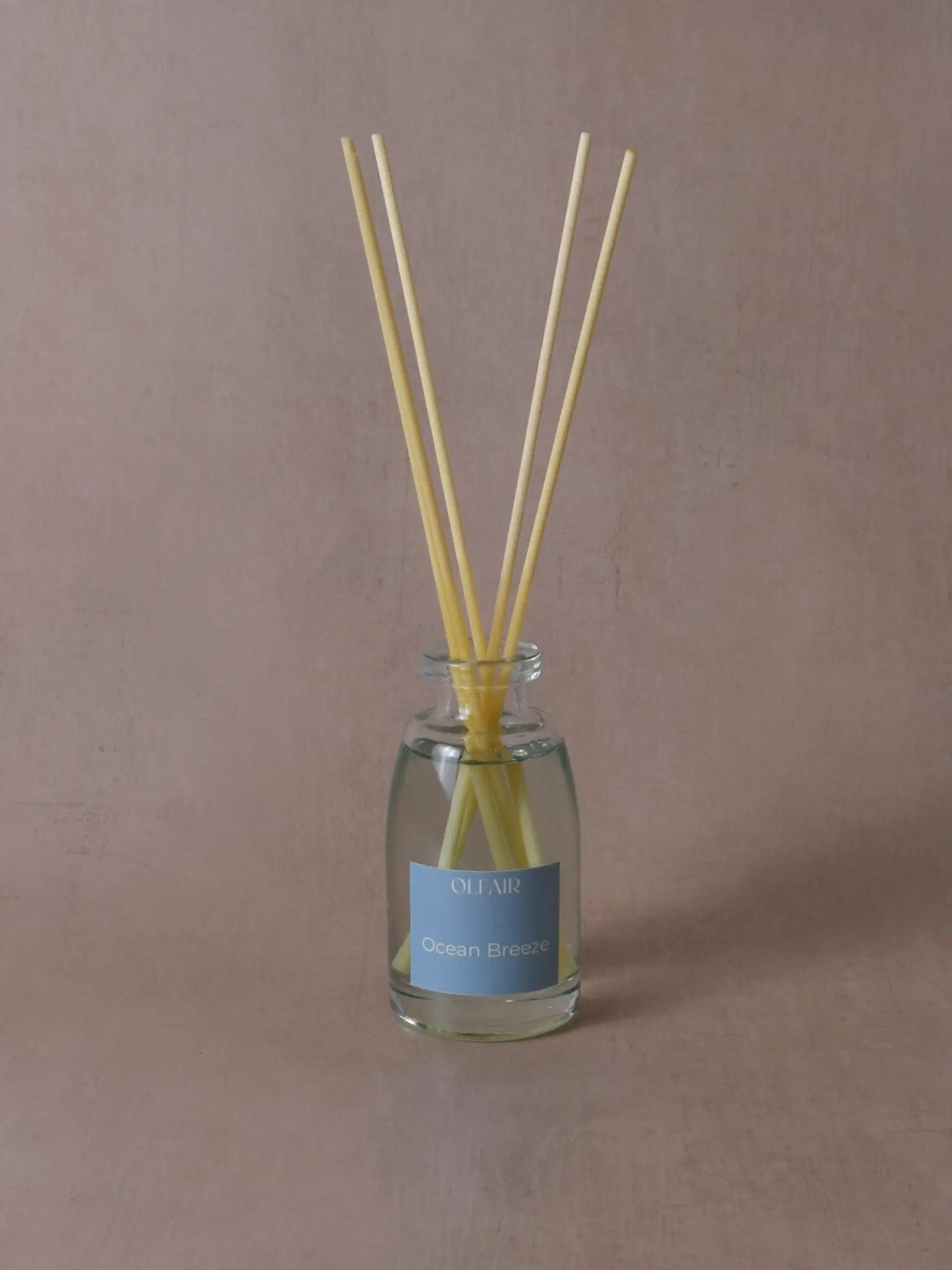 Kleiner Raumduft mit Stäbchen und einem ozeanblauem Etikett vor einem beigen Hintergrund.