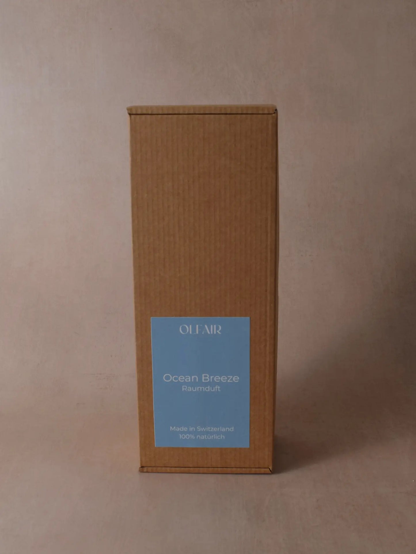 Kartonbox für Raumduft mit ozeanblauem Etikett vor einem beigen Hintergrund.