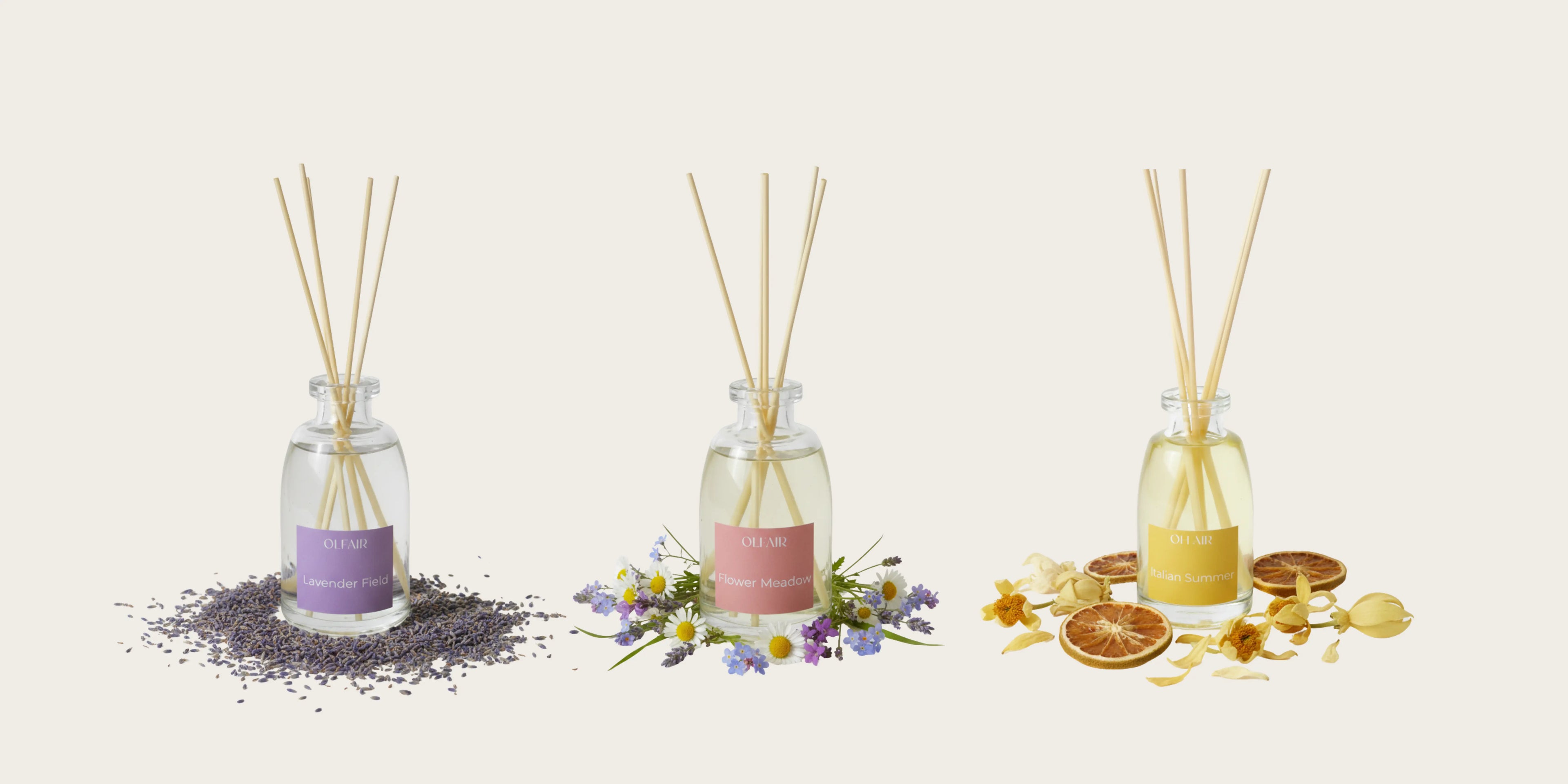 Drei OLFAIR Raumduft-Diffuser nebeneinander vor beigem Hintergrund. Links: 'Lavender Field' mit violettem Etikett und getrocknetem Lavendel. Mitte: 'Flower Meadow' mit rosa Etikett und Wiesenblumen. Rechts: 'Italian Summer' mit gelbem Etikett und getrockneten Orangenscheiben.