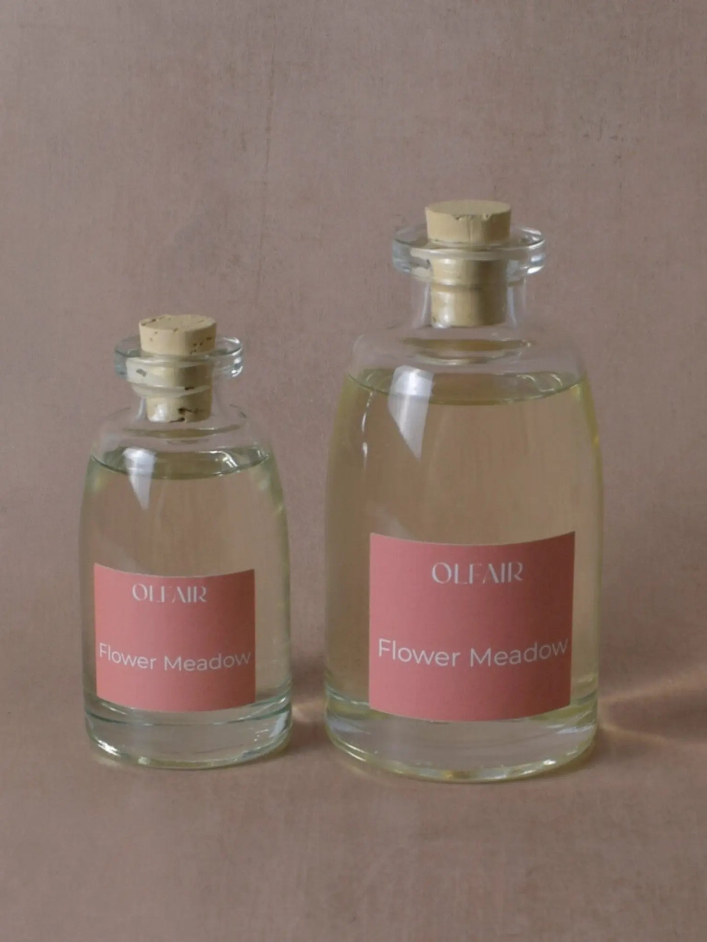 Kleiner und grosser Raumduft mit dunkel rosa Etikett vor einem beigen Hintergrund