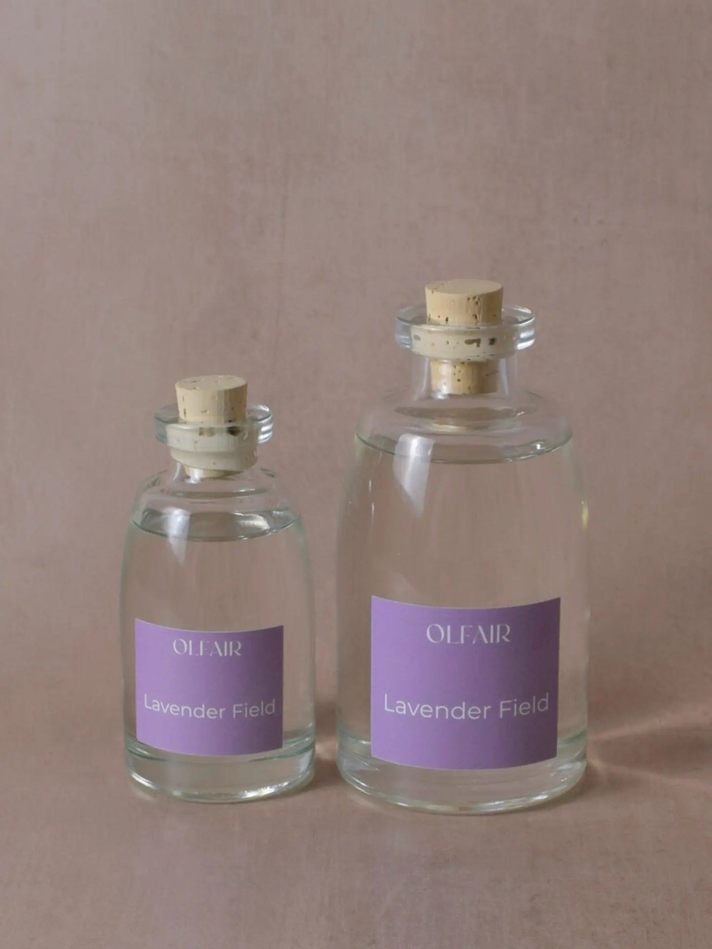 Kleiner und grosser Raumduft mit einem violetten Etikett vor einem beigen Hintergrund.