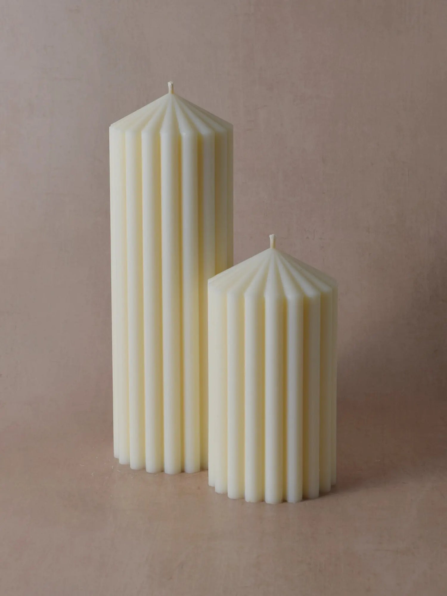 Zwei unterschiedlich grosse Zylinderkerzen mit grossen Rillen vor einem beigen Hintergrund.