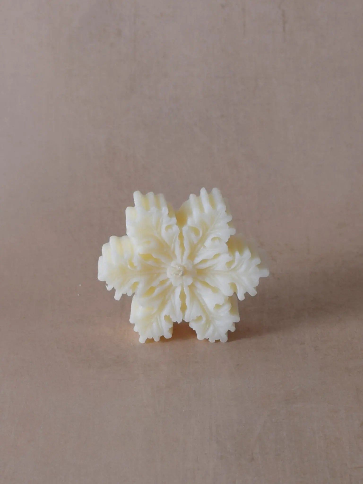 Naturfarbene Kerze in Schneeflockenform.