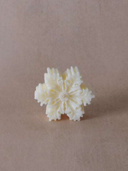 Naturfarbene Kerze in Schneeflockenform.