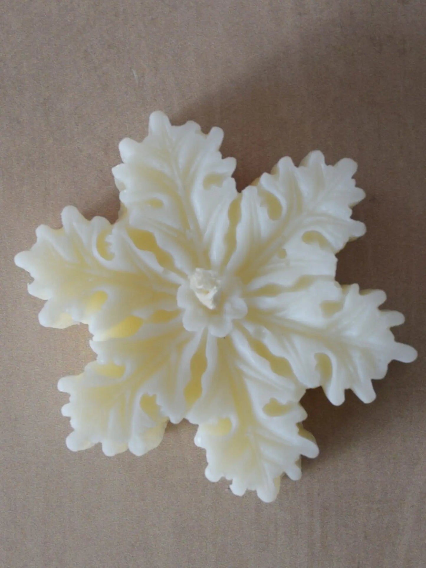 Nahaufnahme einer naturfarbenen Kerze in Schneeflockenform.