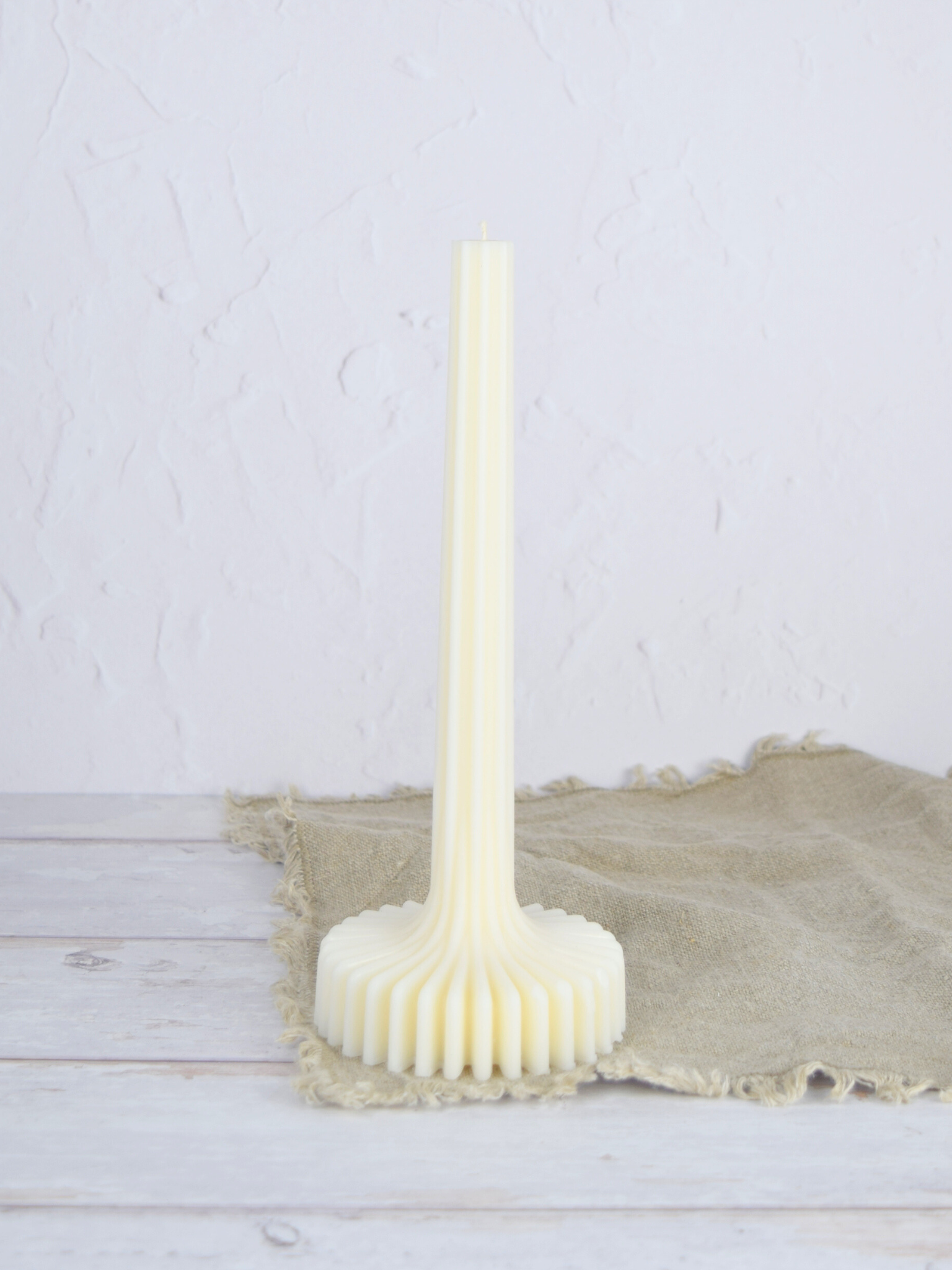Naturweisse Stabkerze mit Sockel auf einem braunen Tuch vor einem weiss Hintergrund