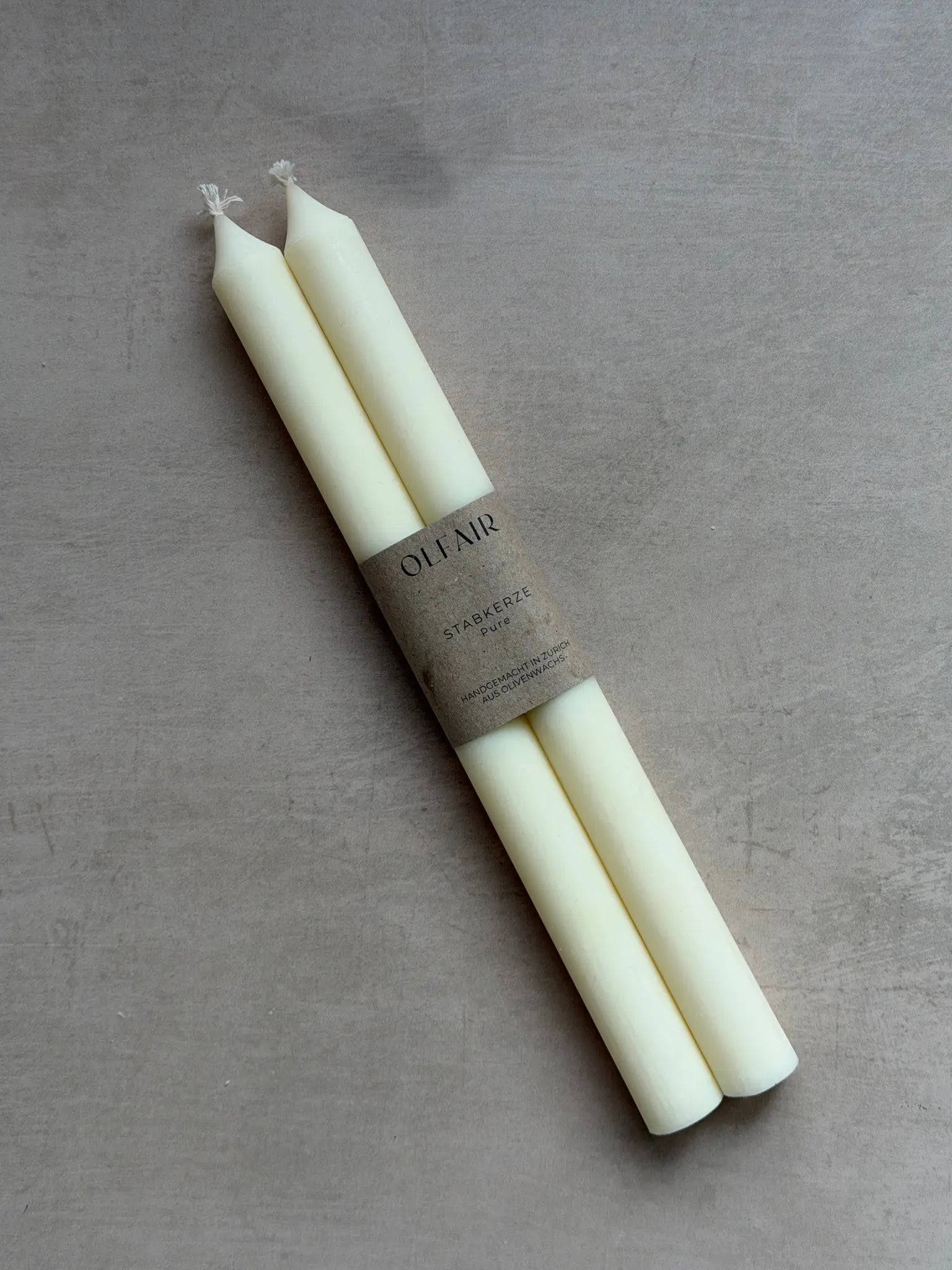 Zwei Stabkerzen in naturweiss vor einem beigen Hintergrund.