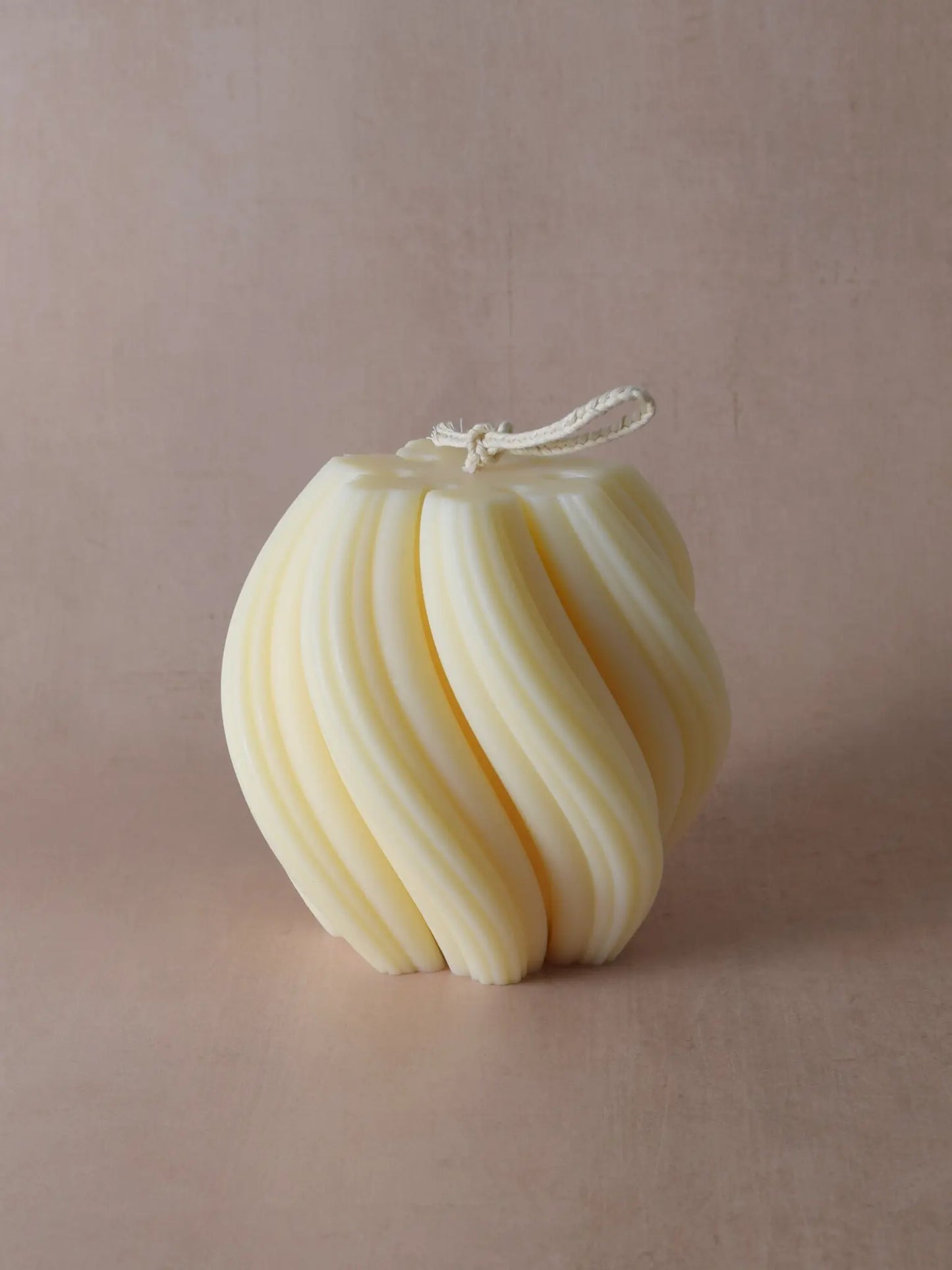 Kerze mit spiralförmiger Struktur vor einem beigen Hintergrund.