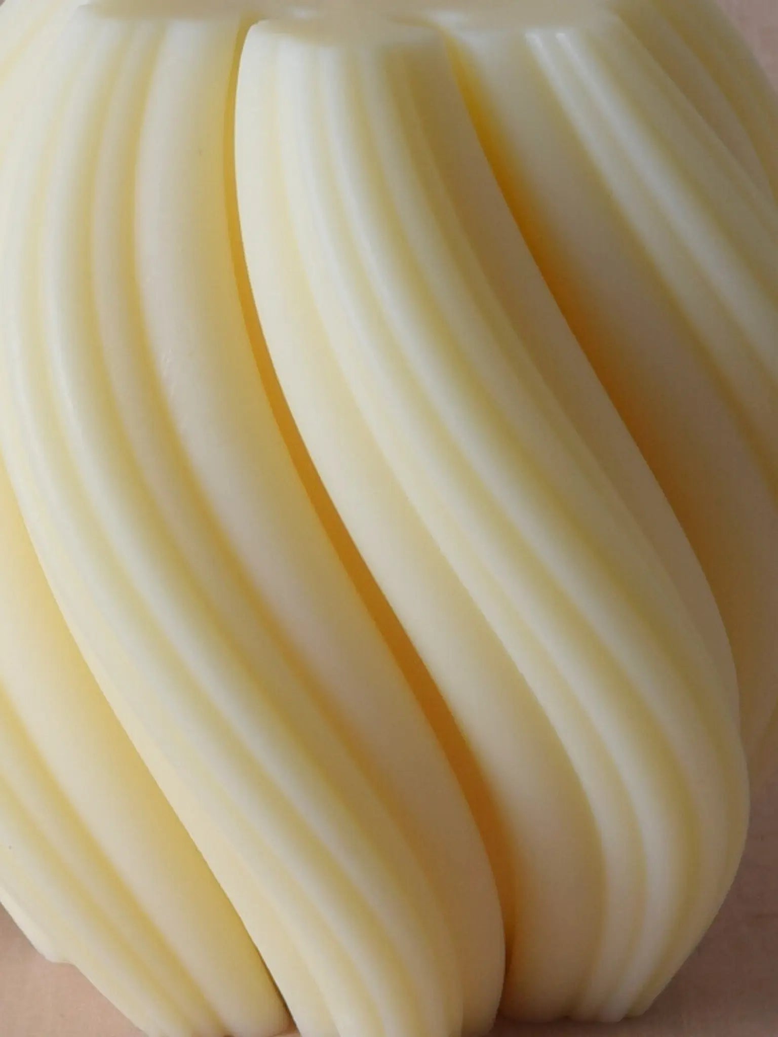 Nahaufnahme einer Kerze mit spiralförmiger Struktur vor einem beigen Hintergrund.