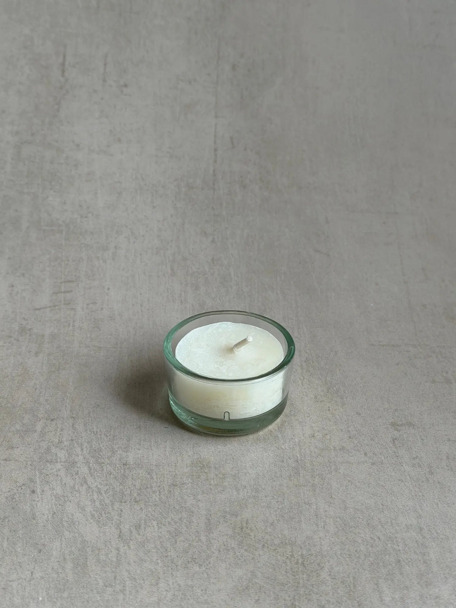 Teelichthülle aus Recyclingglas mit einem Teelicht vor einem beigen Hintergrund