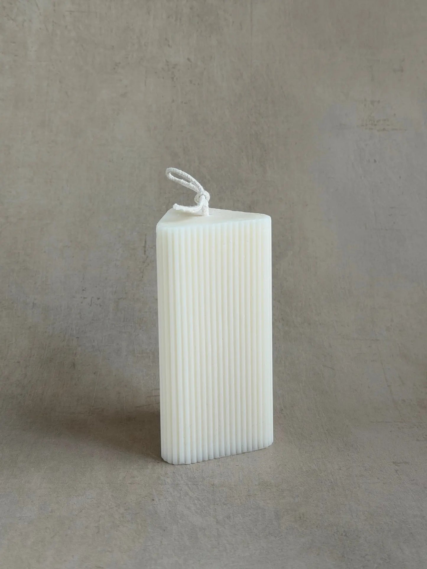 Kleine Kerzen in Dreiecksform mit leichten Rillen auf einem beigen Hintergrund.
