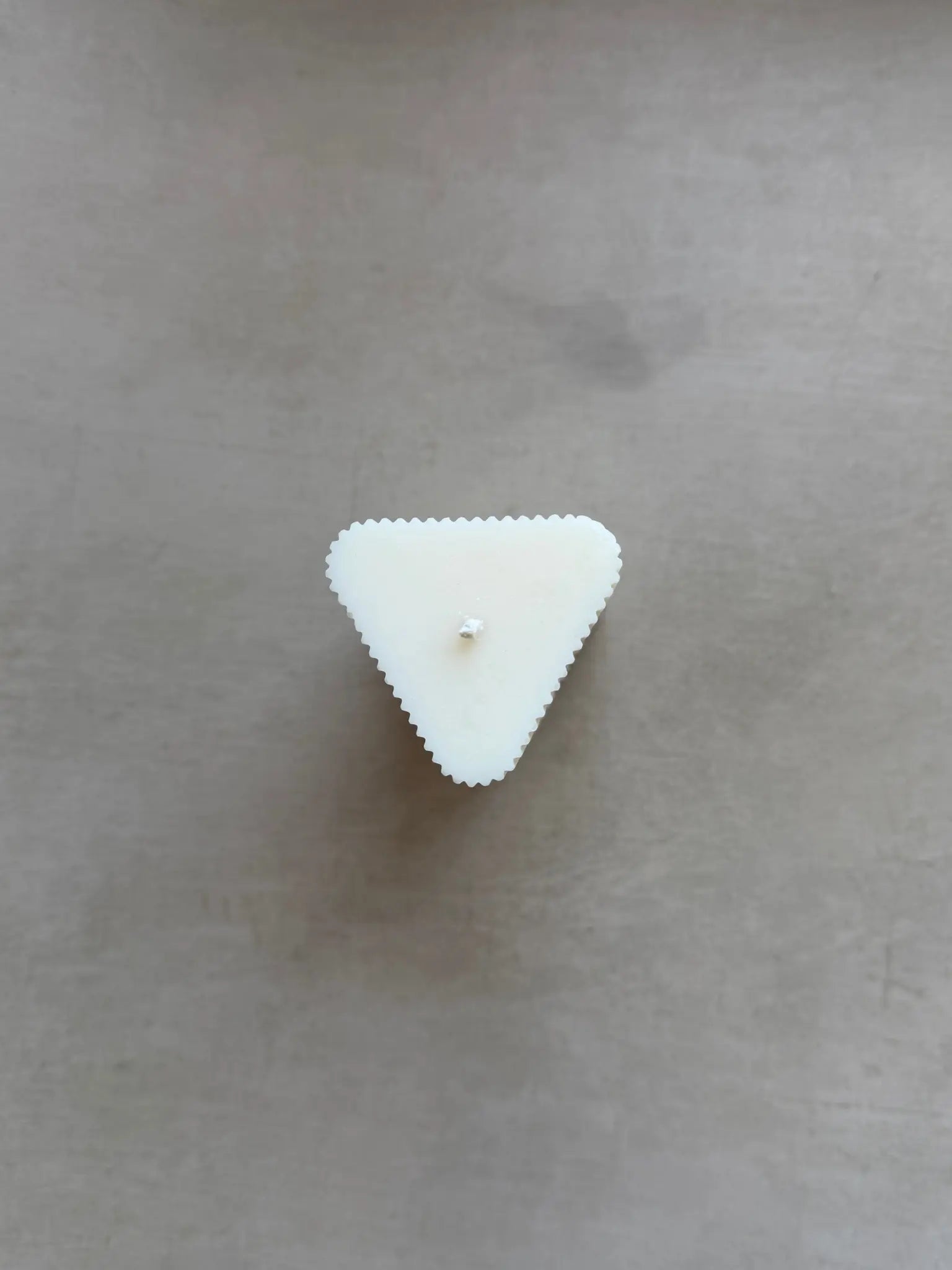 Kleine Kerzen in Dreiecksform mit leichten Rillen von oben auf einem beigen Hintergrund.