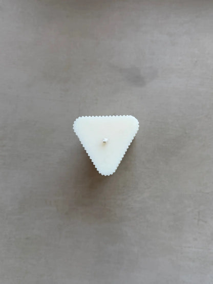 Kleine Kerzen in Dreiecksform mit leichten Rillen von oben auf einem beigen Hintergrund.