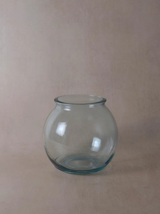 Durchsichtige, runde Vase vor einem beigen Hintergrund
