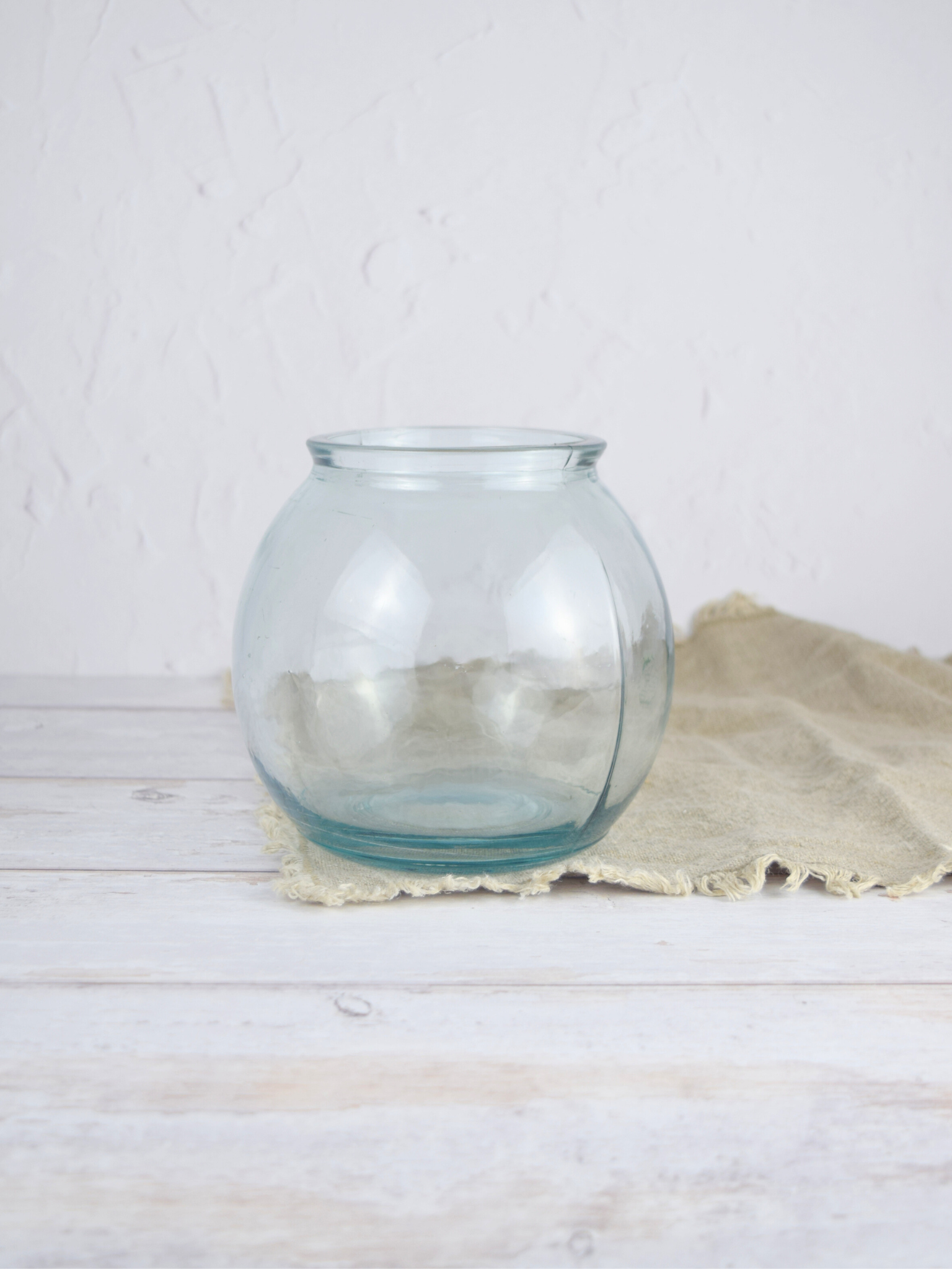 Durchsichtige, runde Vase auf einem braunen Tuch vor einem weissen Hintergrund
