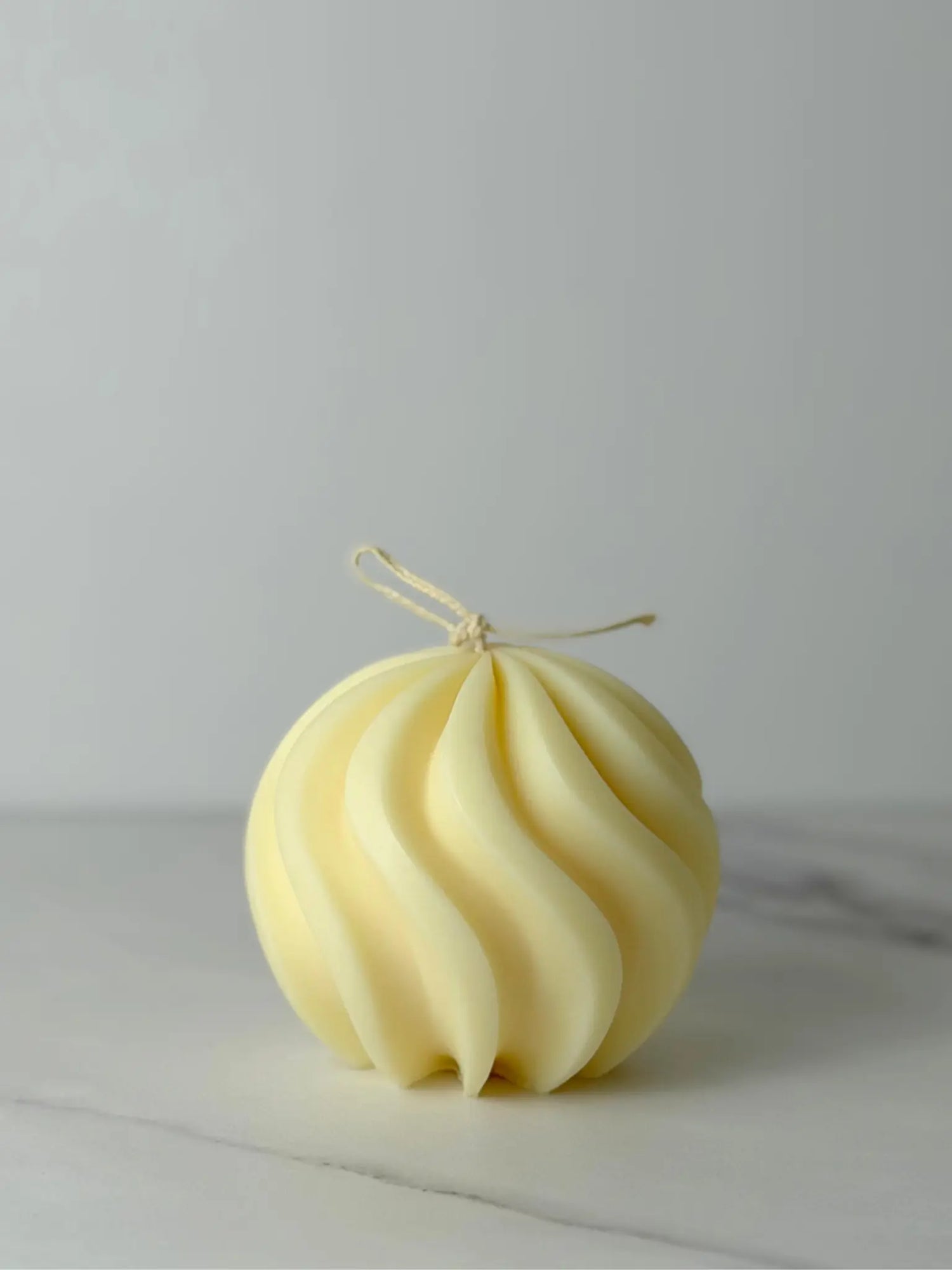 Runde Kerze mit geschwungenen Linien in naturweiss auf einem Marmor Hintergrund