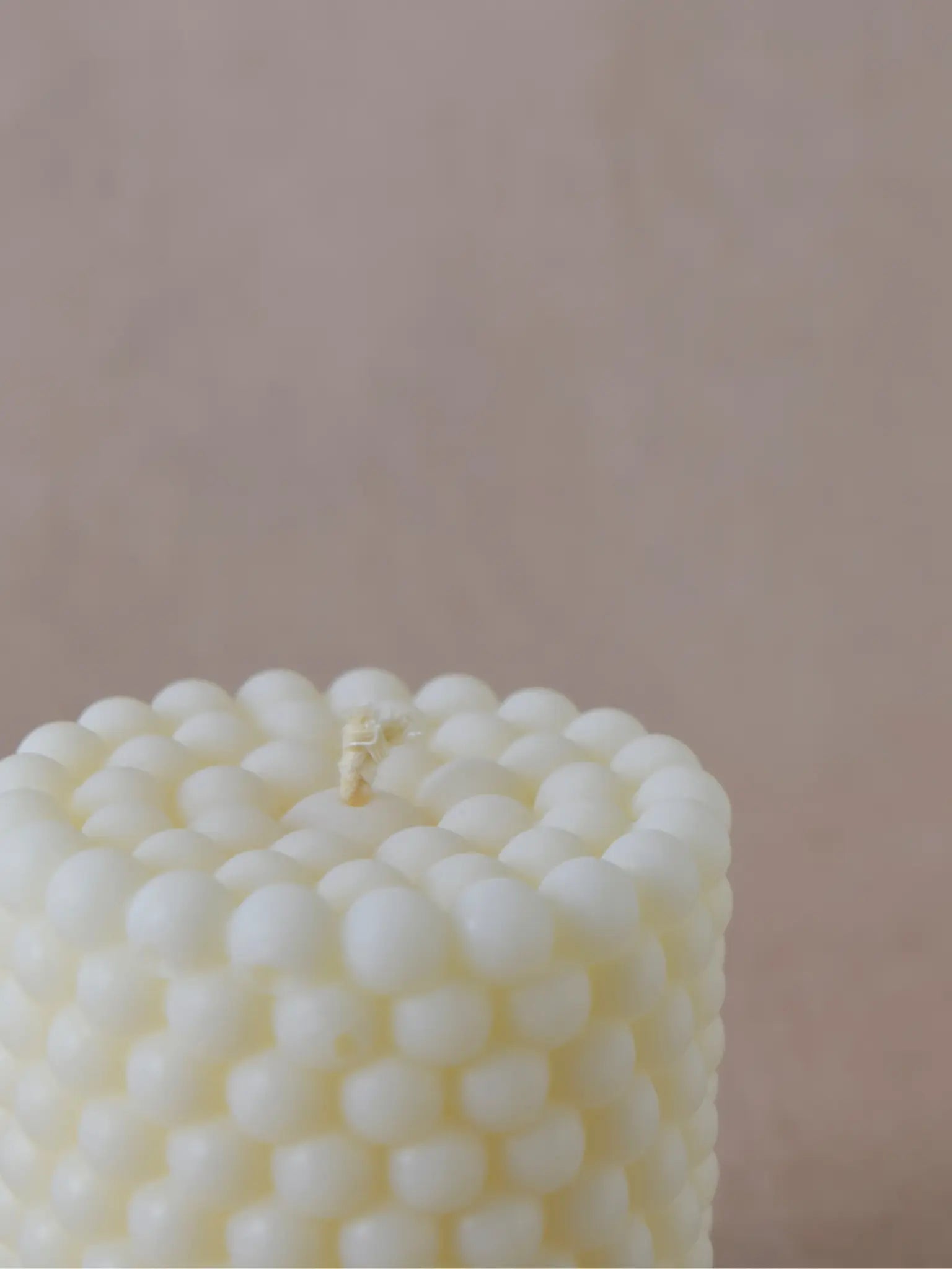 Nahaufnahme einer Zylinderkerze in Bubble-Struktur in naturweiss auf einem   beigen Hintergrund
