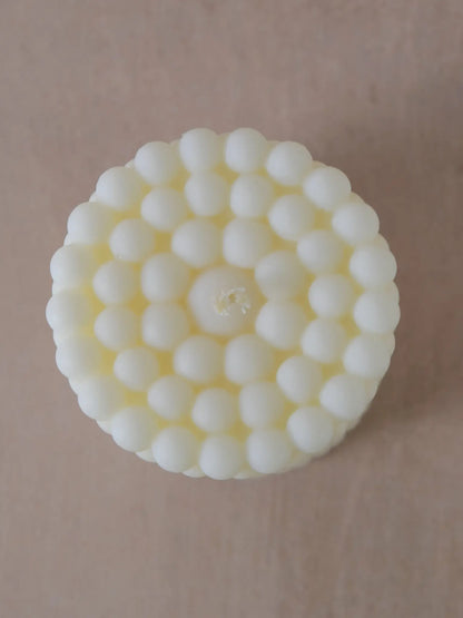 Zylinderkerze in Bubble-Struktur in naturweiss von oben auf einem beigen Hintergrund