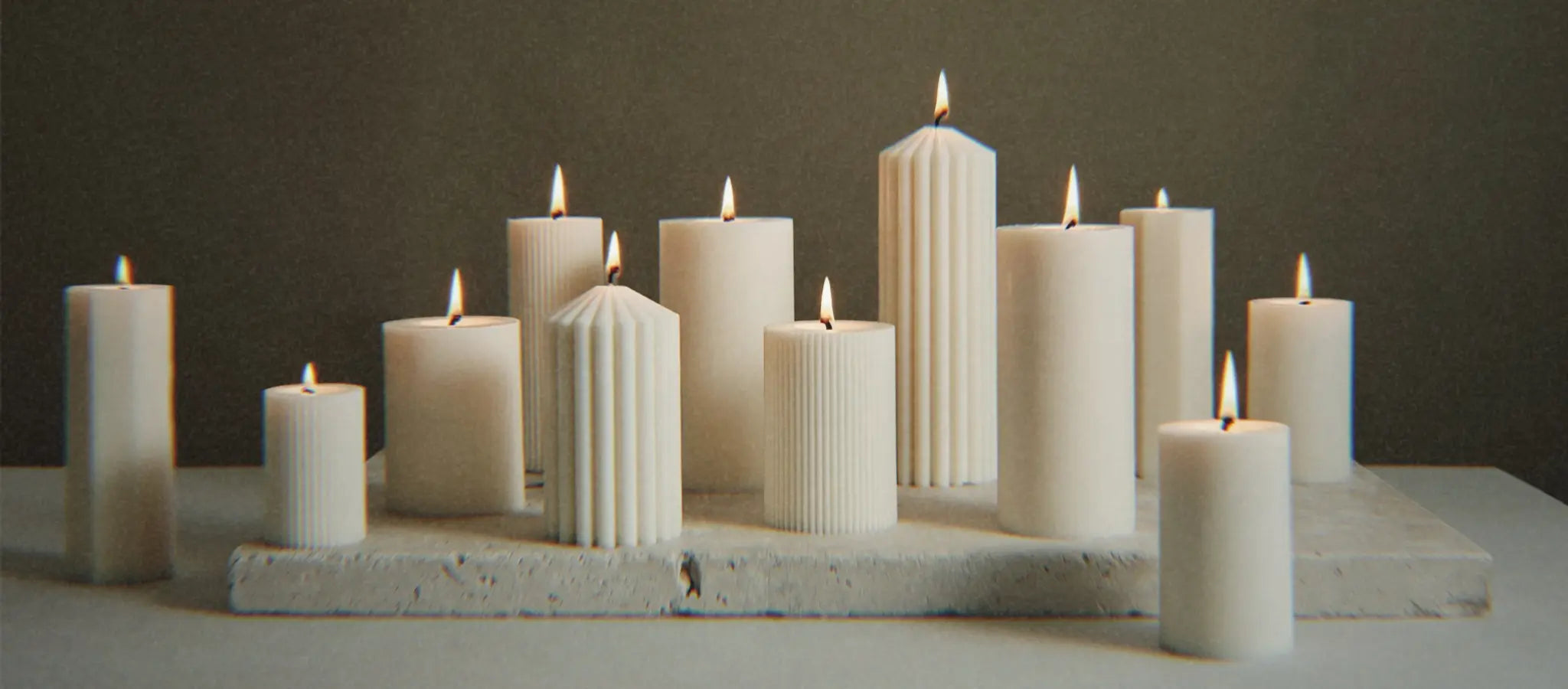 Unterschiedliche Zylinderkerzen auf einem Naturstein. Die Kerzen sind angezündet.